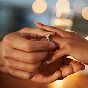 large hands placing engagement ring on smaller hand